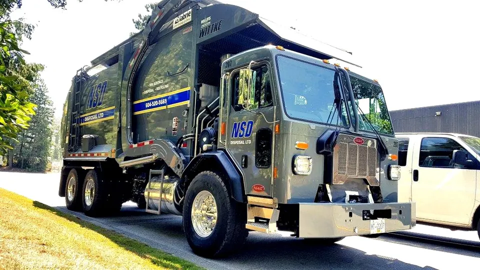 NSD front-load truck with its forks raised, parked beside a white pickup truck