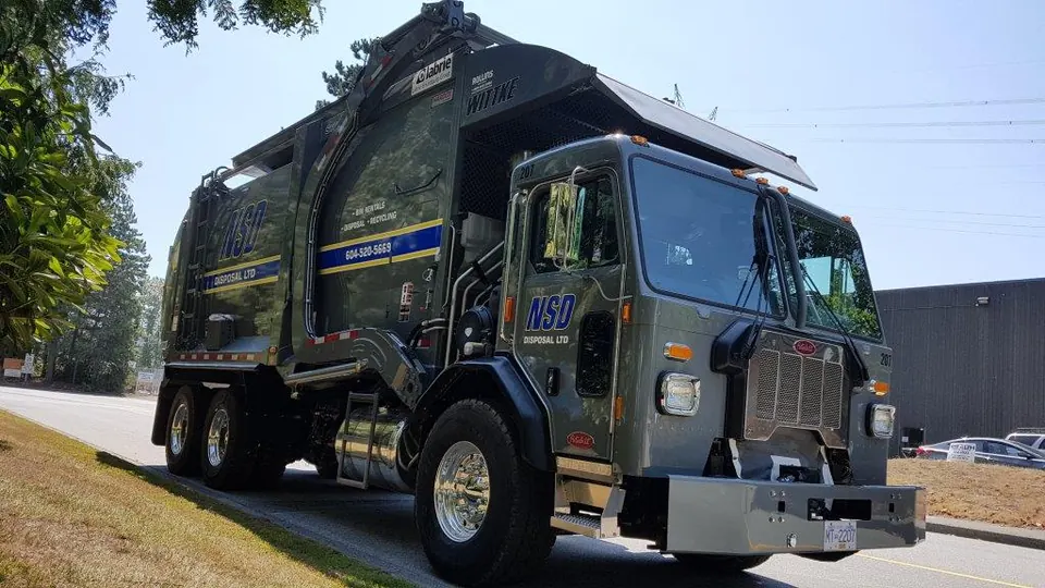 Dark grey NSD Disposal front-load garbage truck parked on a paved lot