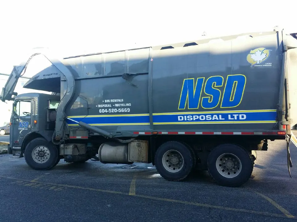 Side view of an NSD Disposal Ltd. front-load truck showing the company logo and phone number